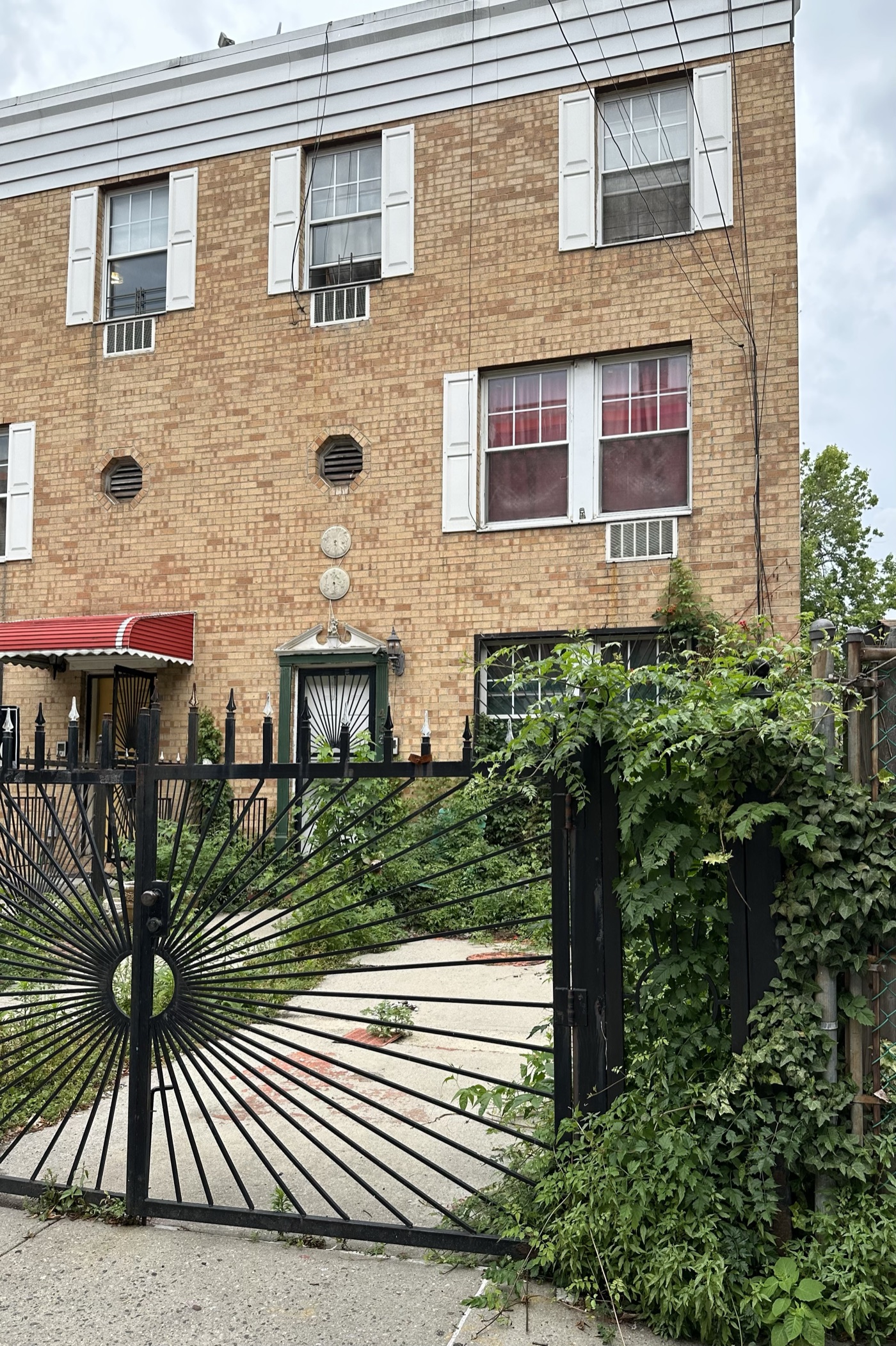 Tan brick two-family house behind a black iron gate, Bronx